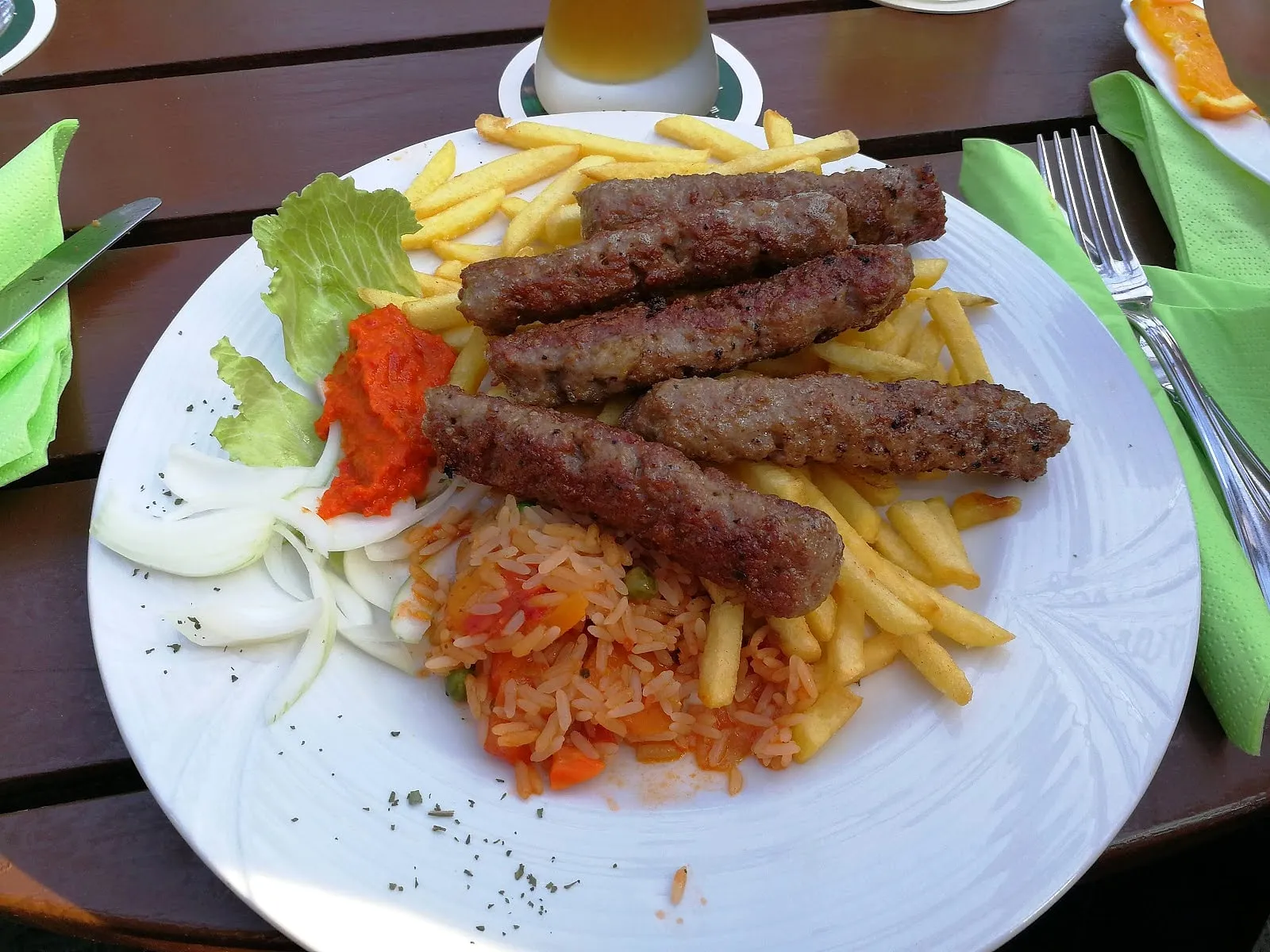 Teller Ćevapčići mit Djuvec-Reis, Ajvar, Zwiebeln und Salat